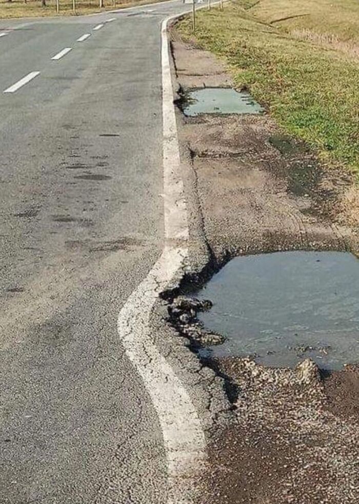 Worn road edge with potholes filled with water, common scene many raised in Eastern Europe can relate to.