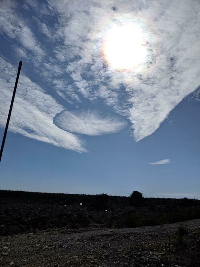 Unphotoshopped sky with unusual circular cloud formation under bright sun over a dark landscape that looks fake but is real.