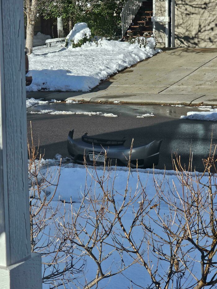 Car bumper stuck in icy, partially melted street, creating an unphotoshopped real picture that looks fake.