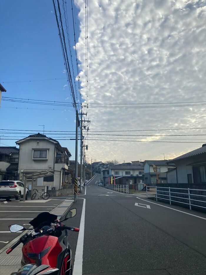 Unphotoshopped photo of a street with half clear blue sky and half dense cloud, creating a surreal real scene.