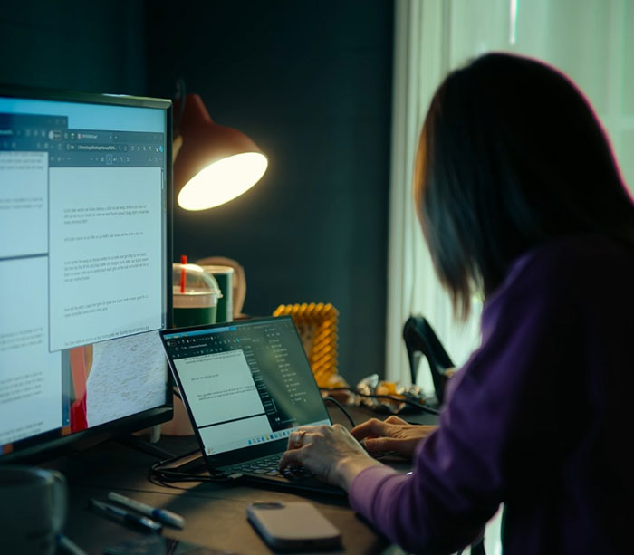 Teen girl working on laptop and monitor in dimly lit room, related to catfish and obsessed mom story.