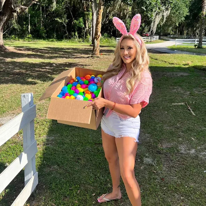 Model posing outdoors holding a box of colorful balls, wearing bunny ears and casual summer clothing, big breasts discrimination.