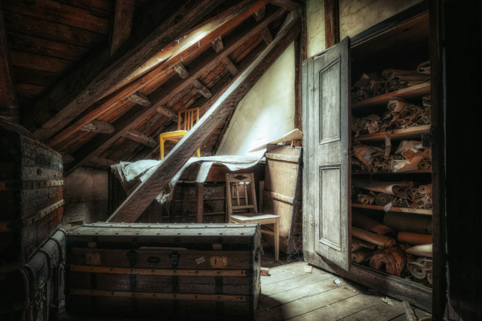 Dimly lit attic filled with old trunks and shelves of rolled papers, evoking a sense of hidden secrets and horror stories.