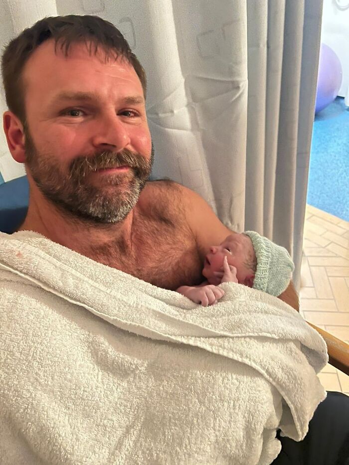 Man holding newborn baby wrapped in towels, sharing a tender wholesome moment in a calm indoor setting.
