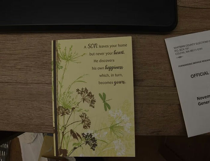 Greeting card on a wooden desk with text and a document nearby, related to Bryan Kohberger's mom discussing Idaho crimes.