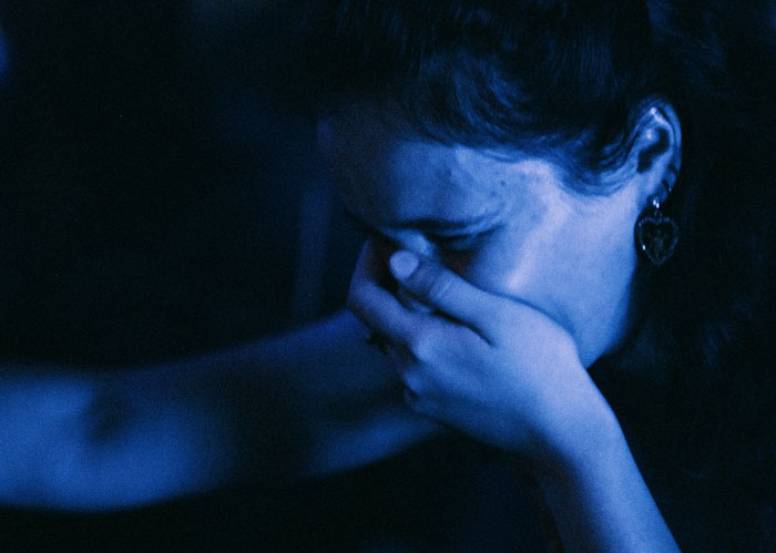 Woman in dark blue lighting covering her mouth with a hand, conveying fear and unease related to security guards creepy experiences.