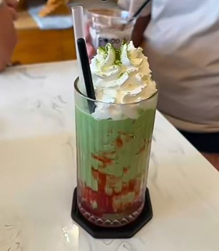 Iced matcha drink topped with whipped cream and a black straw on a table, highlighting matcha health concerns.
