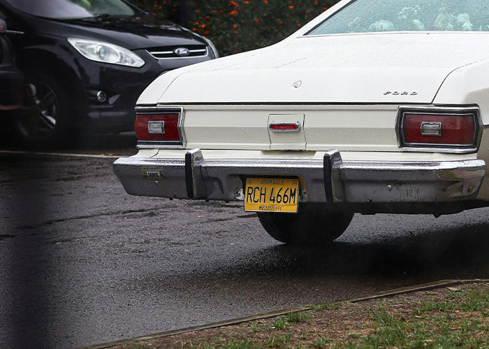 White Ford car with a bent license plate on a wet road, illustrating one of the criminal fails caught on camera.