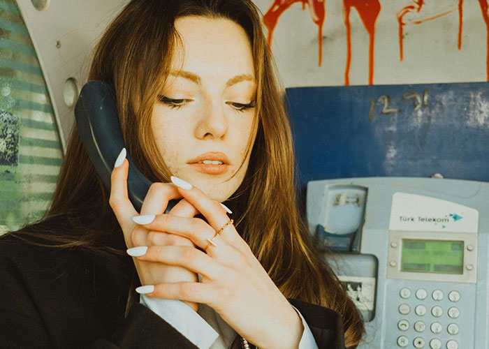 Young woman using a public phone with a distressed expression, surrounded by eerie red stains in a dimly lit space.