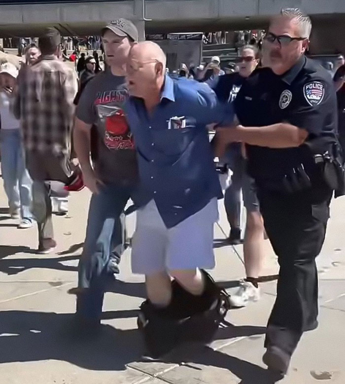 Police officer detaining a man who falsely confessed to being Charlie Kirk's assassin in a crowded outdoor setting. Police officer detaining a man who falsely confessed to being Charlie Kirk's assassin in a crowded outdoor setting.