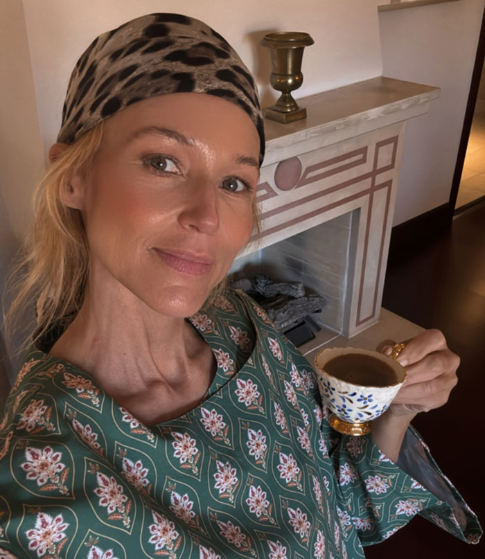 51-year-old 90s star with toned body wearing headscarf and patterned top, holding cup, sharing fitness secrets at home.