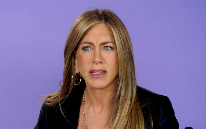 Jennifer Aniston reacting with surprise during an interview about learning Reese Witherspoon's real name after 25 years.