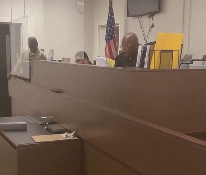 Courtroom scene with officials discussing the case of a teacher arrested for using poop spray around school.