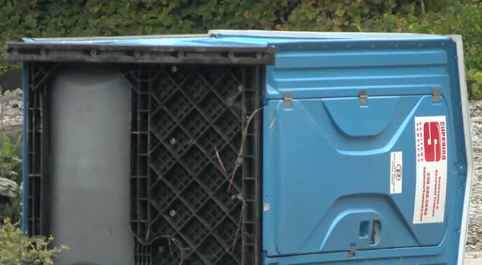 Blue porta-potty lying on its side outdoors, linked to a cop shooting incident involving teens over prank dispute.