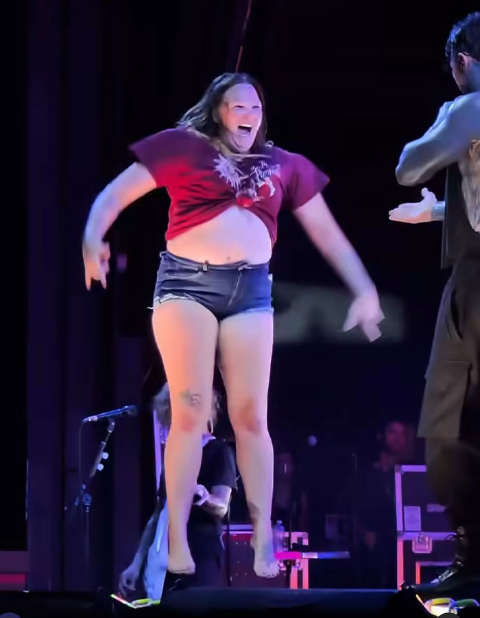 Woman rushing the stage at concert, captured mid-jump in casual outfit, highlighting fat shaming controversy with ex-con rock star.