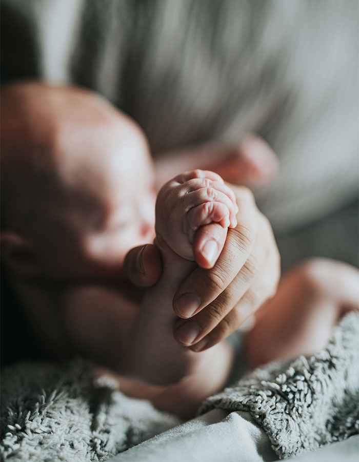 Newborn baby held gently in adult hands, symbolizing delicate care in disturbing cheerleader case news.