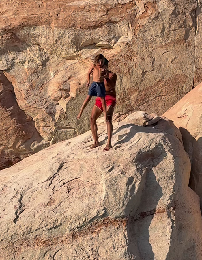 Man holding young boy on a large rock near a cliff, related to viral outrage about tough love dad incident. Man holding young boy on a large rock near a cliff, related to viral outrage about tough love dad incident.