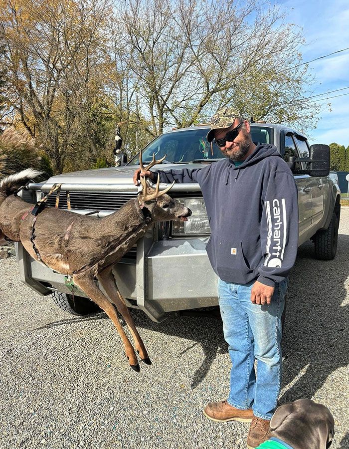 Man in casual clothing standing beside truck, holding a deer with antlers, related to Michigan suspect's eerie confession.