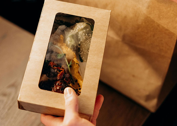 Hand holding a packaged food item in a cardboard box, illustrating common purchases ditched due to high price tags.