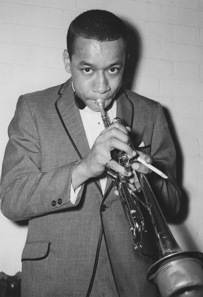 Black and white photo of male celebrity playing trumpet in a suit, representing male celebrities involved in tragic events.