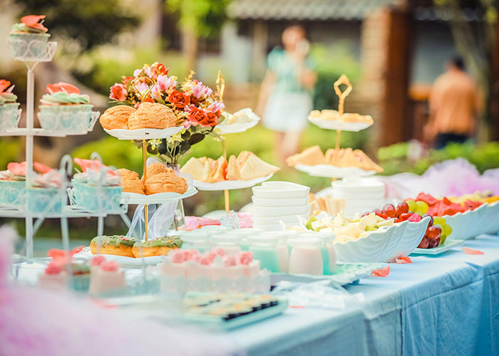 Baby shower table with sandwiches, desserts, fruit, and floral centerpiece in an outdoor setting.
