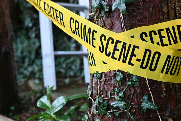 Yellow crime scene tape wrapped around a tree trunk, marking a restricted area for police investigation.