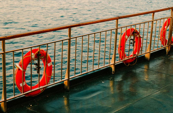 View of safety rings attached to metal railing on a boat deck with water in the background, related to security guards.