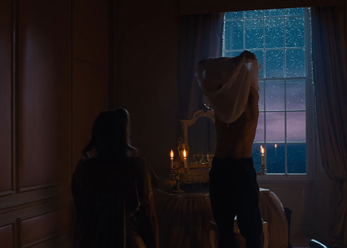 Dimly lit 1800s bedroom scene with Margot Robbie and Jacob Elordi, candles glowing near a window under a starry night sky.