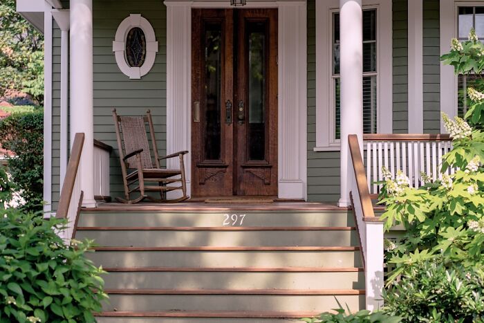 Front porch of a house with wooden rocking chair and stairs, representing a food delivery driver’s chaotic story location.