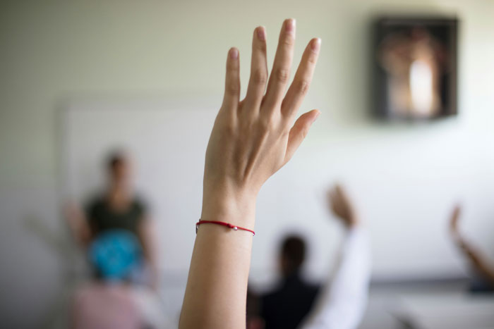 Raised hand in classroom setting showing engagement, illustrating real-life cheat codes for better sleep and problem-solving.