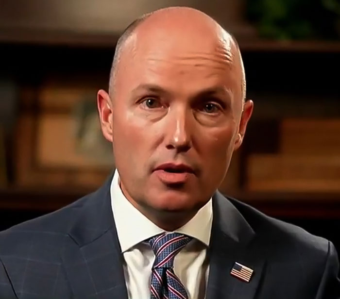 Man in suit with an American flag pin, serious expression, representing FBI revealing DNA evidence in Tyler Robinson case.
