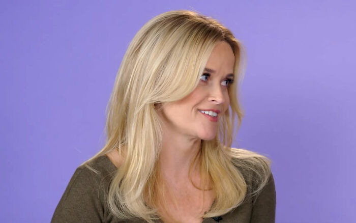Blonde woman smiling and looking to the side against a purple background in a Jennifer Aniston Reese Witherspoon context.