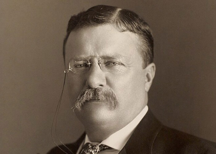 Portrait of a historical figure wearing glasses and suit, representing significant events with societal damage impact.