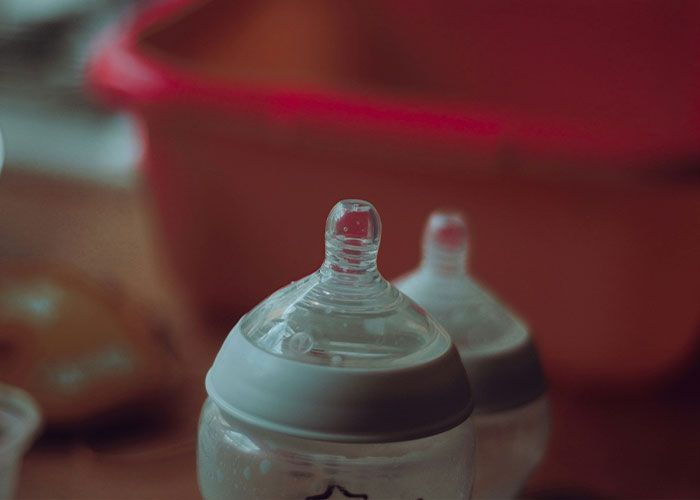 Baby bottles with nipples in soft focus, highlighting breastfeeding and breast milk pumping challenges.