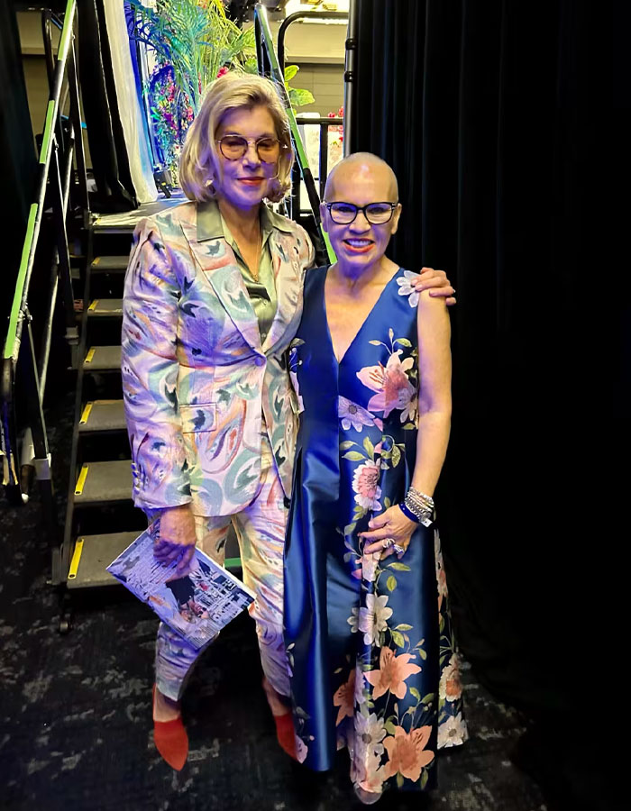 Two women, one in a floral suit and the other in a floral dress, standing together highlighting cancer diagnosis symptoms awareness.