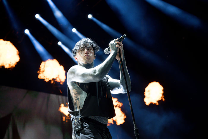 Ex-con rock star performing on stage with microphone while flames burst in the background during live concert.