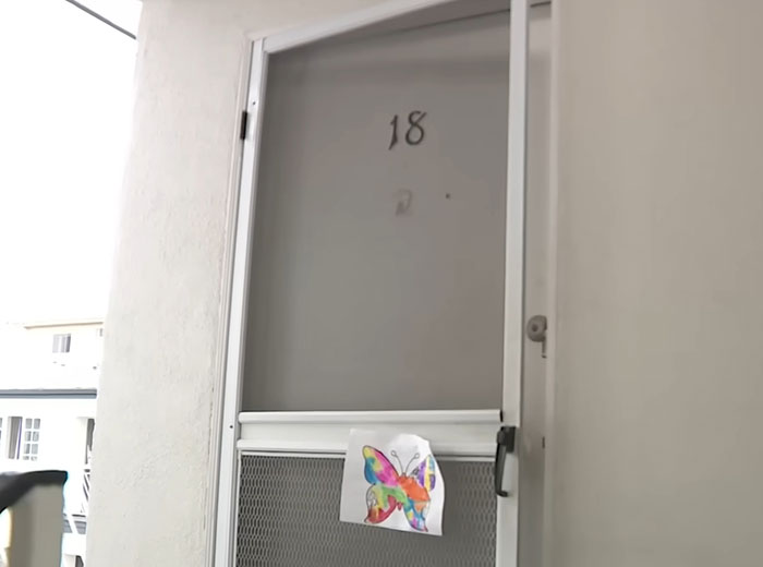 Apartment door number 18 with a colorful butterfly drawing taped, related to American Nightmare mom found lifeless at home.