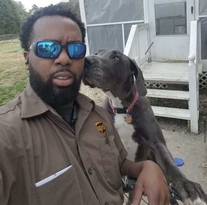 UPS driver wearing sunglasses takes selfie with an adorable dog showing affection during delivery visit outside a home.
