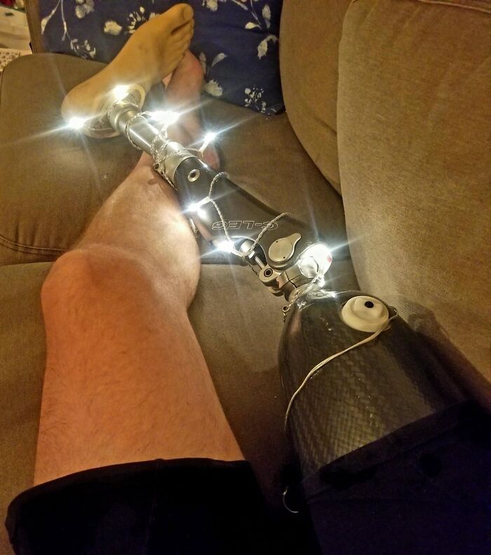 Person with a high-tech prosthetic leg wrapped in string lights relaxing on a couch for wholesome posts distraction.