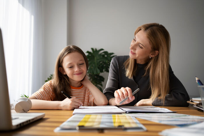 A woman teaching a young girl with notebooks and pens, sharing life-changing sentences and meaningful lessons.