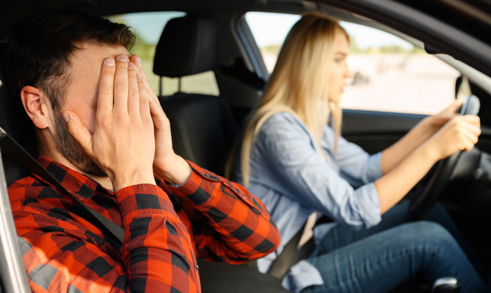 Man covering his face in distress while woman drives car, illustrating woman giving husband another chance lesson.