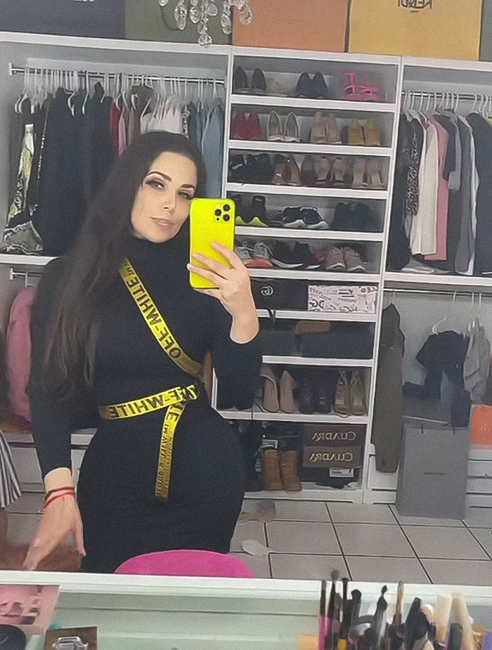 Influencer Esmeralda Ferrer Garibay taking a mirror selfie in a black outfit with yellow strap in a closet full of clothes and shoes. Influencer Esmeralda Ferrer Garibay taking a mirror selfie in a black outfit with yellow strap in a closet full of clothes and shoes.