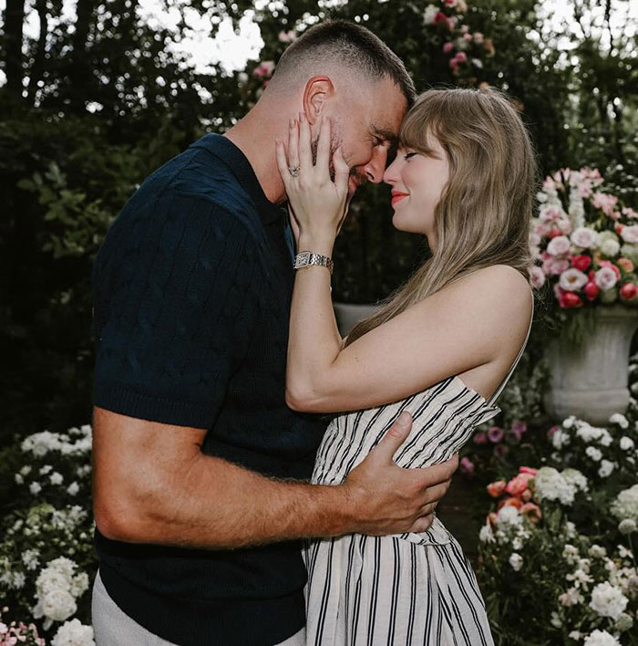 Travis Kelce and Taylor Swift embracing closely outdoors surrounded by flowers, highlighting Travis Kelce&rsquo;s answer about Taylor Swift.