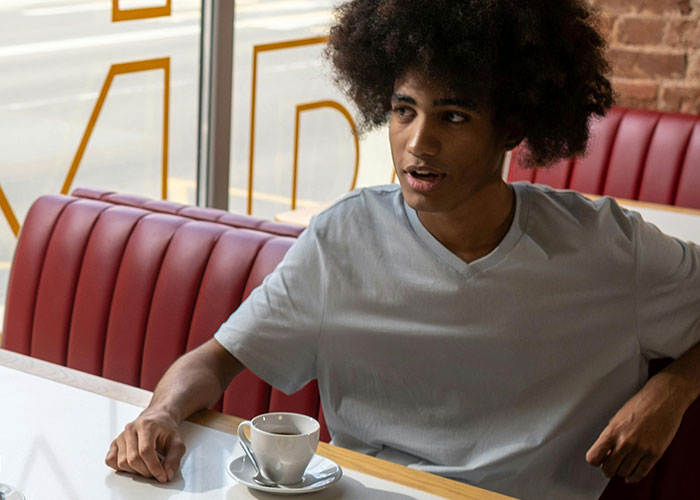 Young man sitting in a cafe booth with a coffee cup, illustrating incredible coincidences that sound fake but are true.