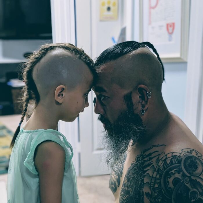 Man with tattoos and beard touching foreheads with young girl in a tender moment, showcasing wholesome connection and love.