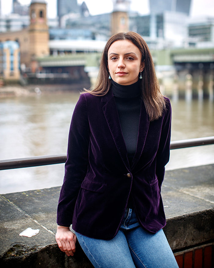 Young woman in purple blazer standing near river, related to story about doctor finding hair and teeth inside instead of pregnancy.