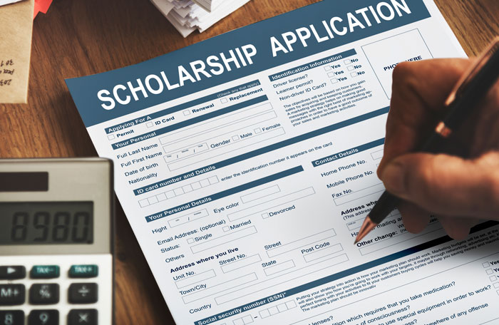 Person filling out a scholarship application form with a pen, next to a calculator showing the number 8980.
