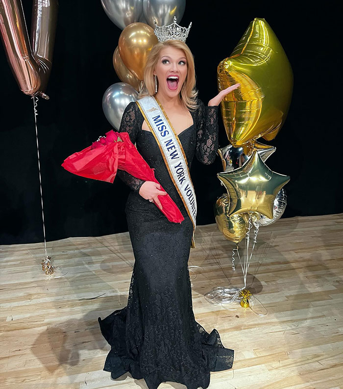 Newly crowned Miss America in black gown and crown holding flowers with celebratory balloons in the background. Newly crowned Miss America in black gown and crown holding flowers with celebratory balloons in the background.