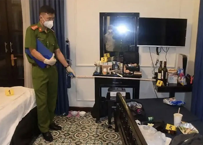 Police officer in a room investigating the scene related to poisoned limoncello causing tragic deaths of a newly engaged couple.