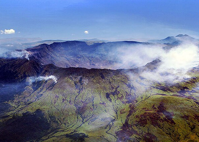 Volcanic eruption smoke rising over green mountainous landscape showing historical event damage to society.